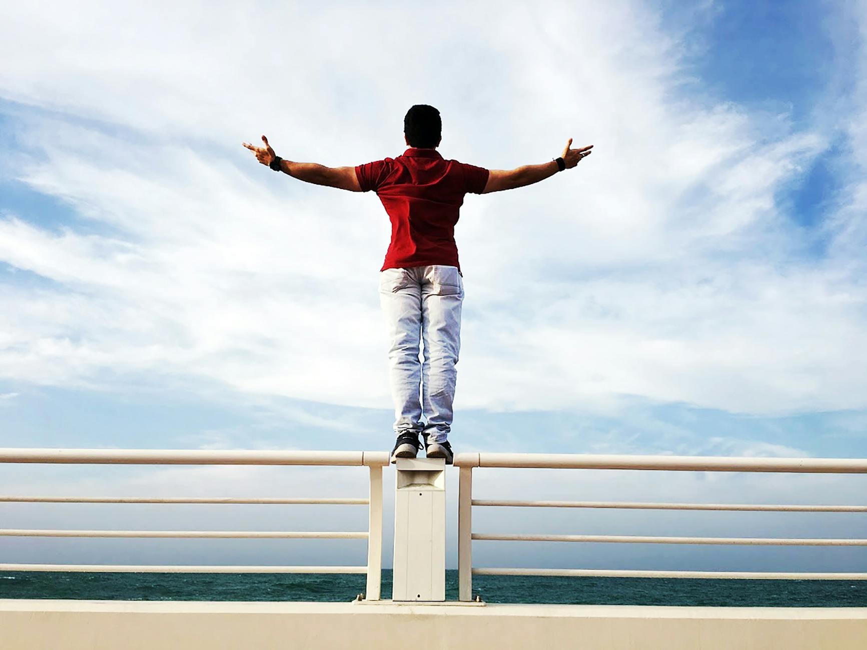 person raising hands mid air sidewards while standing on gray steel railings